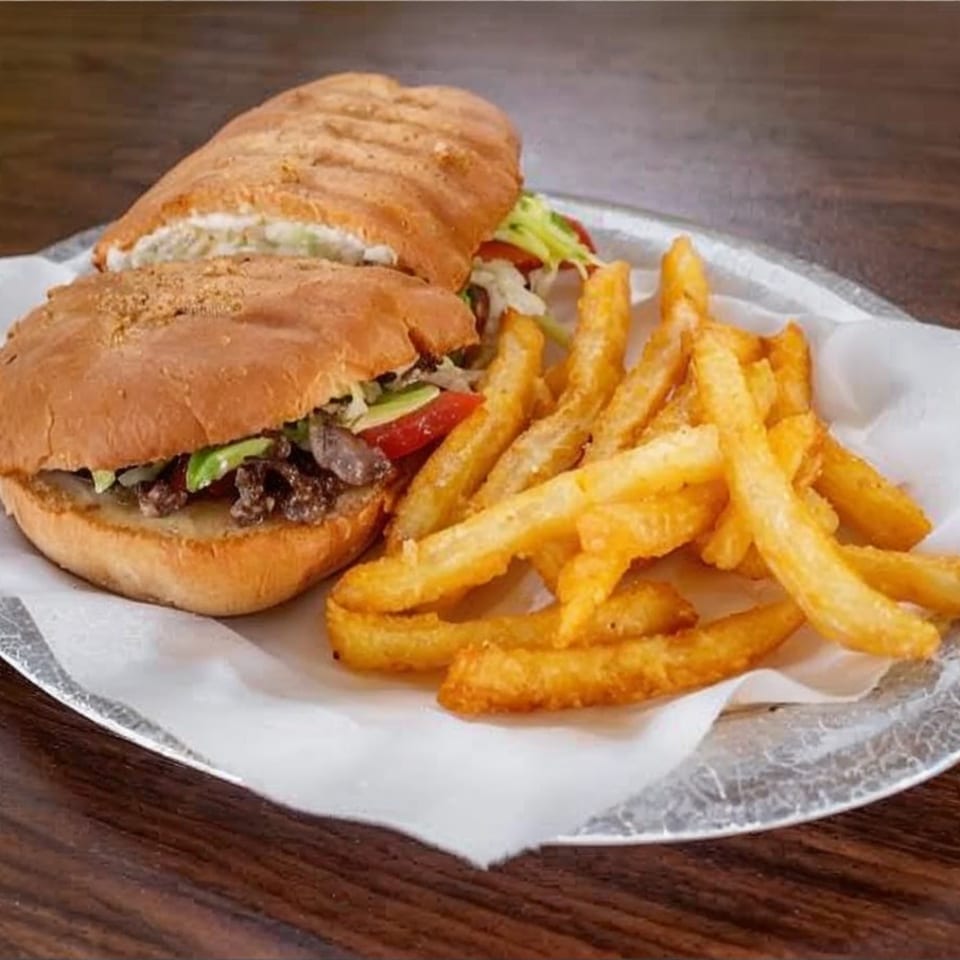 A Mexican torta sandwich with steak, avocado, and vegetables, served with a side of golden french fries.