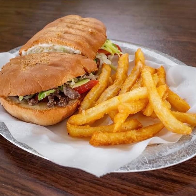 A Mexican torta sandwich with steak, avocado, and vegetables, served with a side of golden french fries.