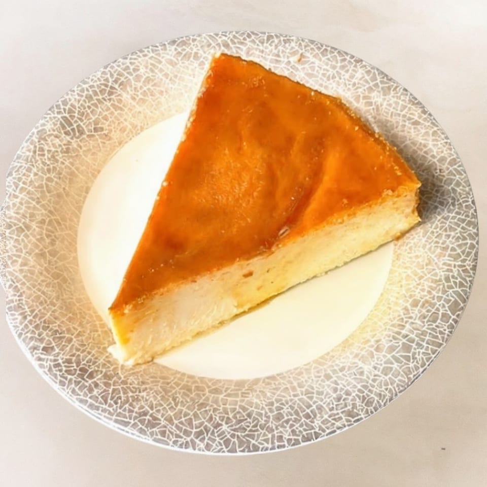A slice of golden-brown flan with a creamy custard base on a decorative white and gray plate.