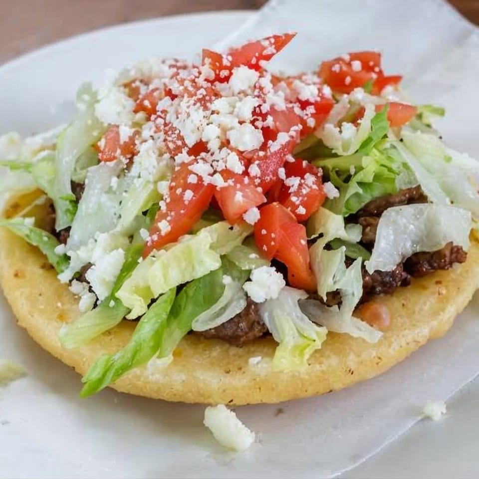 A La Perla Tapatia sope topped with seasoned meat, shredded lettuce, diced tomatoes, and crumbled cheese.